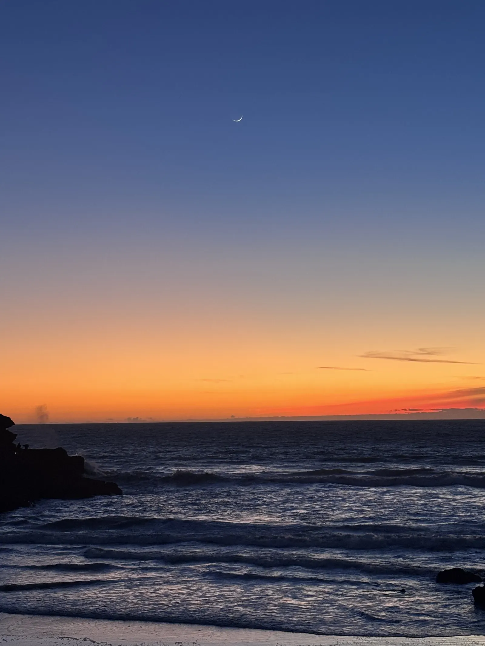 Un croissant de lune au-dessus de la côte, à la tombée de la nuit