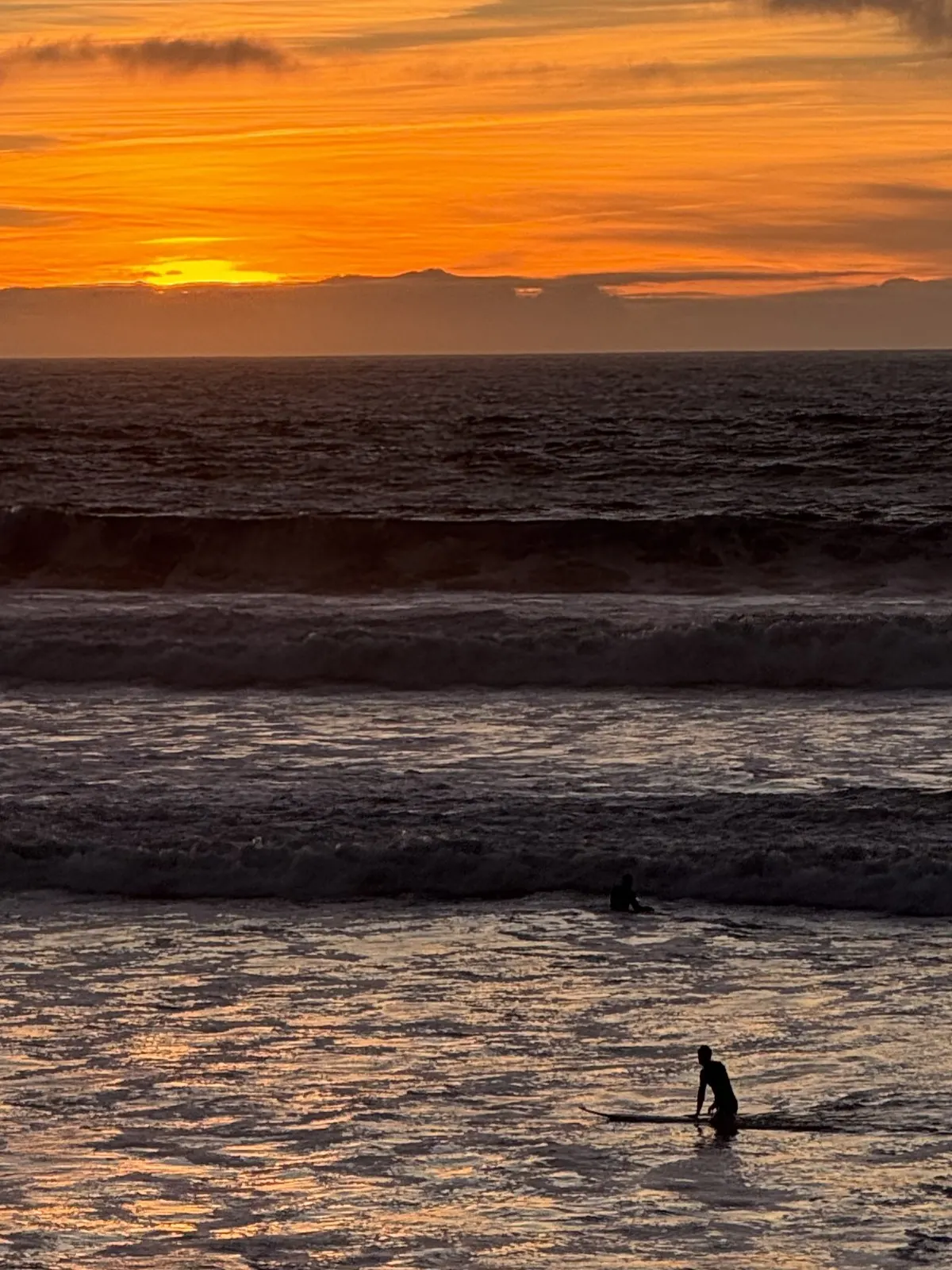 Un surfeur seul dans l'océan, à contre-jour du couchant